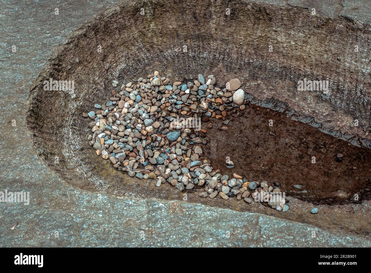 Des pierres abstraites se dispersent sur la surface d'une flaque, créant une réflexion hypnotique. Les formes déformées et les couleurs éclatantes se fondent. Banque D'Images