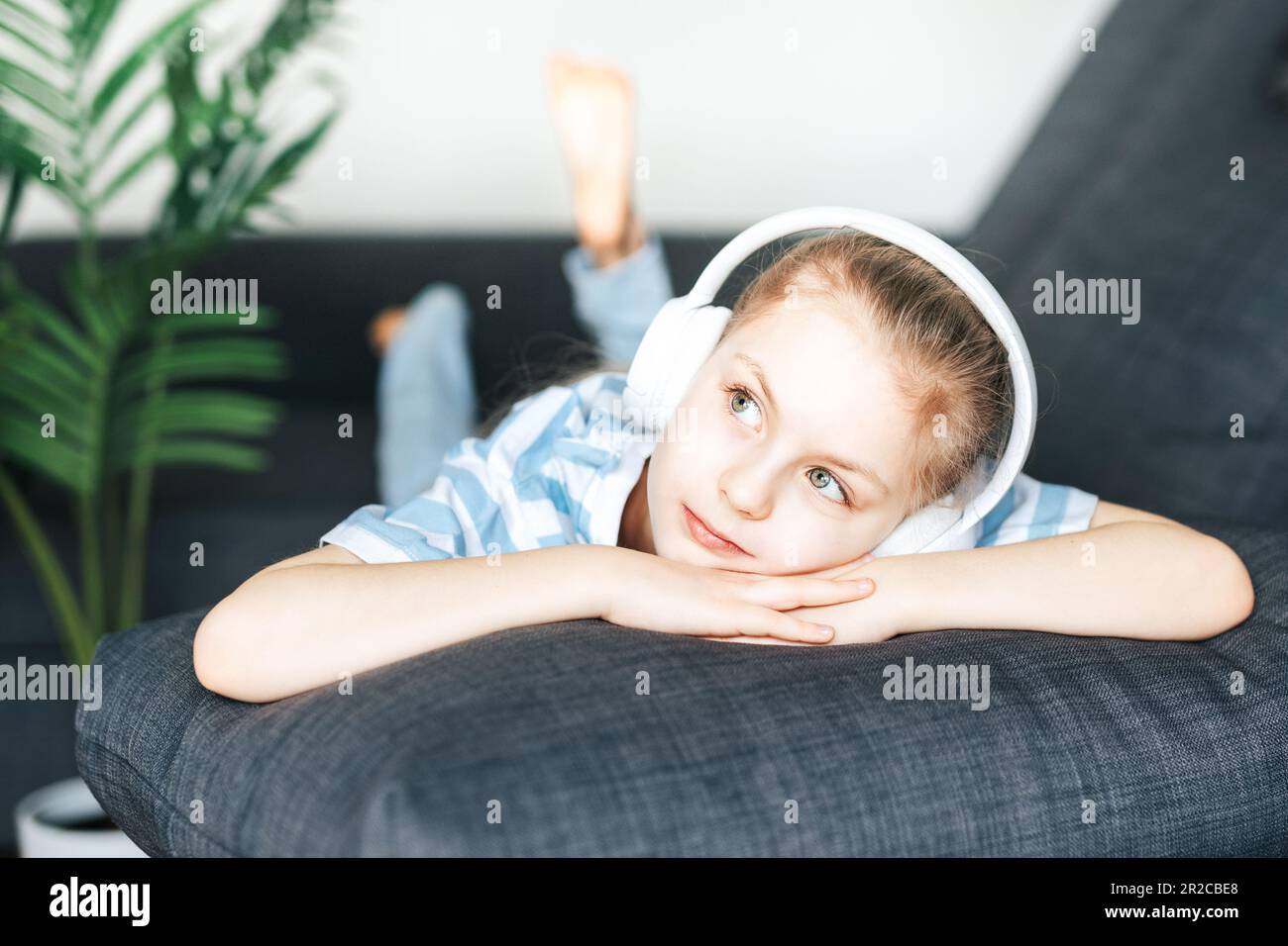 Une petite fille mignonne qui écoute de la musique dans un casque tout en étant allongé sur le canapé à la maison. Banque D'Images