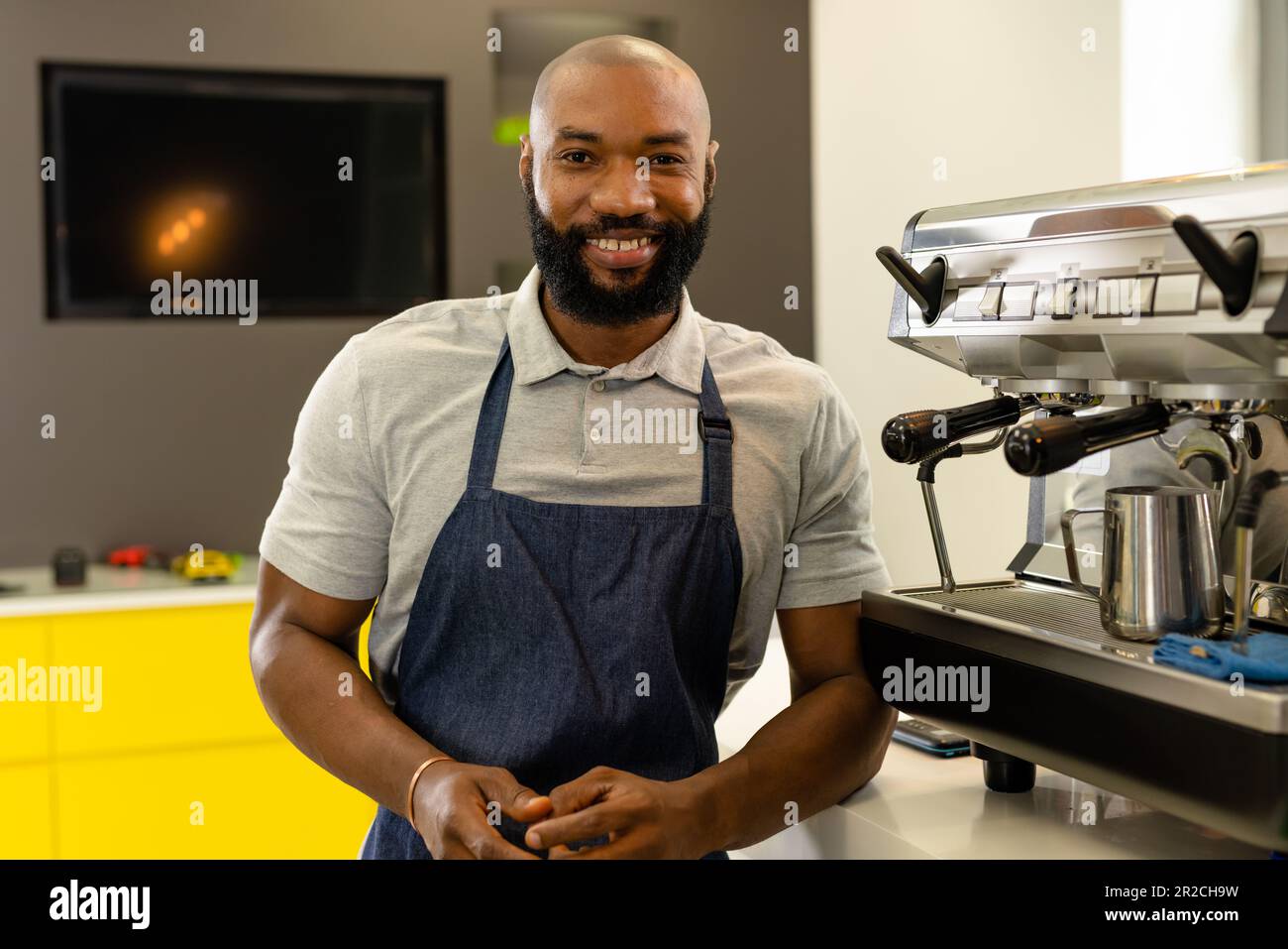 Portrait d'un barista américain d'afrique barbu en tablier, debout près de la cafetière, au café-restaurant Banque D'Images