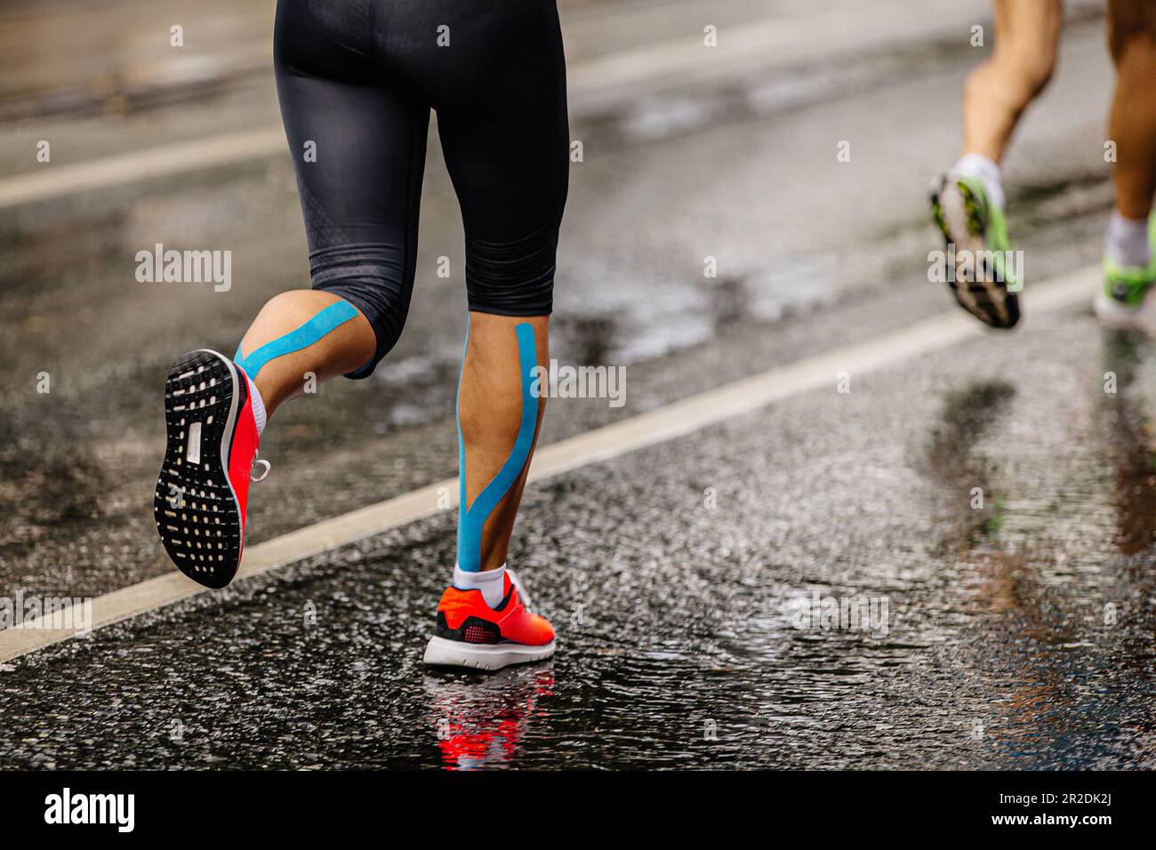jambes athlète féminine coureur course marathon sur asphalte humide, ruban kinésio bleu sur shins Banque D'Images