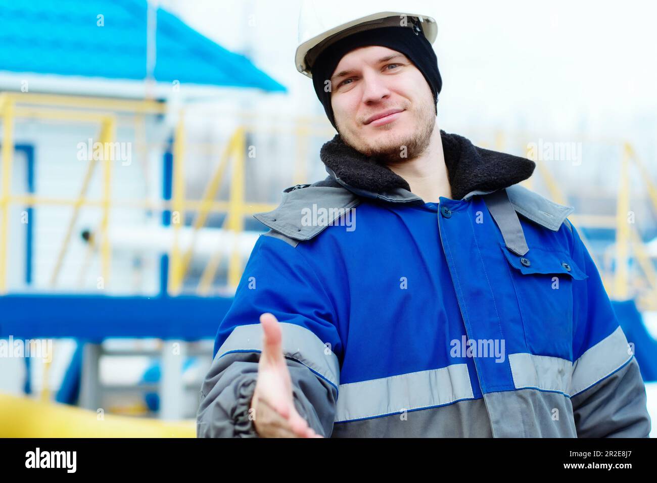 Invitation à une équipe de professionnels du gaz. Un jeune ingénieur en gaz, en casque et en pelage de pois d'hiver, étend sa main vers l'avant pour saluer. Attitude positive. Travailleur caucasien authentique. Banque D'Images