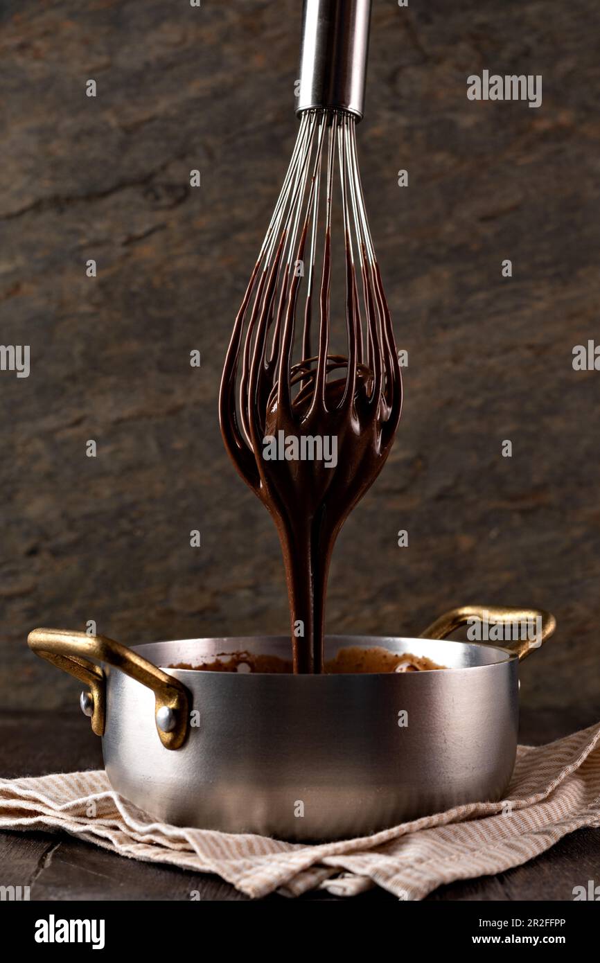 Crème de chocolat liquide dans une louche à l'aide d'un fouet. Arrière-plan sombre Banque D'Images