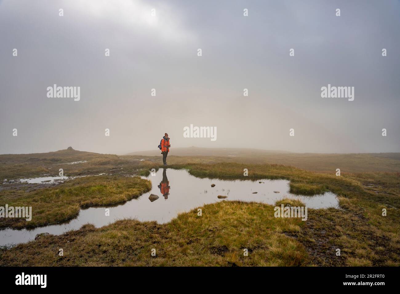 Le randonneur se trouve sur une surface d'eau lisse et symétrique dans la lande haute des îles Klakkur, Klaksvík et Féroé. Banque D'Images