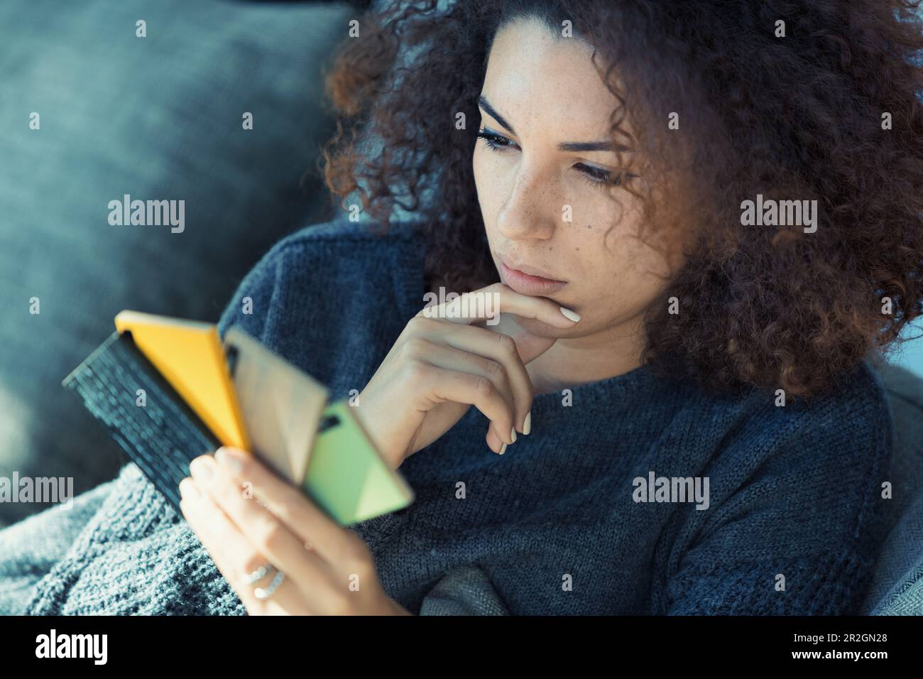 Une femme à l'aspect ethnique et aux cheveux bouclés, belle avec des dents parfaites, aime choisir des meubles ou des couleurs de sol à partir de nuances sur son canapé. Elle est une Banque D'Images