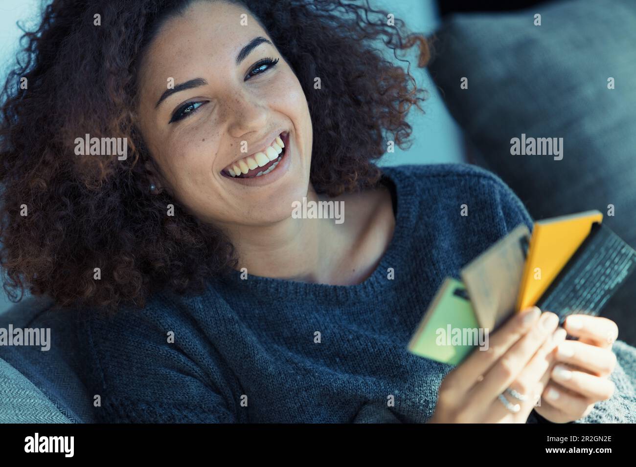 Belle femme aux cheveux bouclés, présentant des dents parfaites et un look ethnique, sélectionne les couleurs des nuances pour la décoration de la maison, fortement absorbée et excitée Banque D'Images