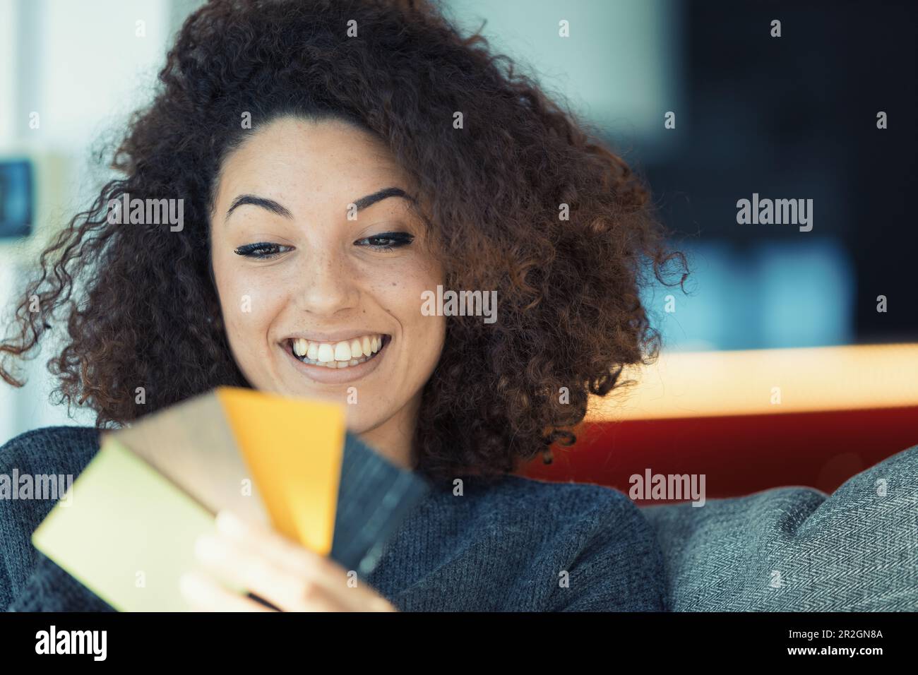 Femme à l'apparence ethnique et aux dents parfaites, choisit avec enthousiasme des échantillons de couleur sur son canapé, enthousiaste à l'idée de personnaliser son style de vie. Elle Banque D'Images