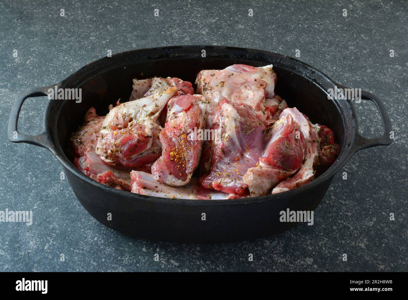 Viande d'agneau assaisonnée dans une marmite en fer noir, prête à rôtir, sur fond de pierre sombre, vue latérale Banque D'Images