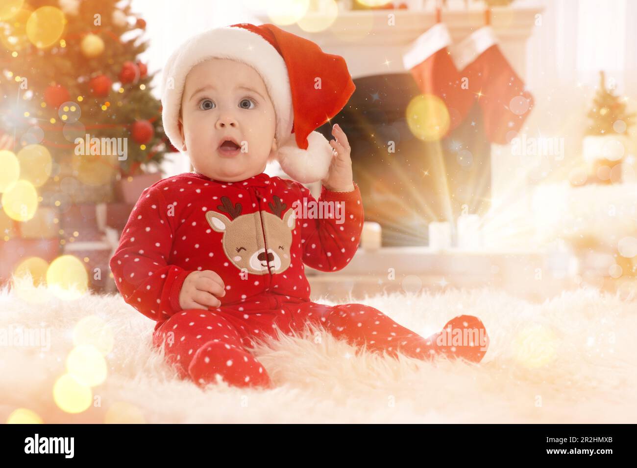 Bébé en chapeau de père Noël et pyjama de Noël lumineux au sol à la maison.  Atmosphère festive magique Photo Stock - Alamy