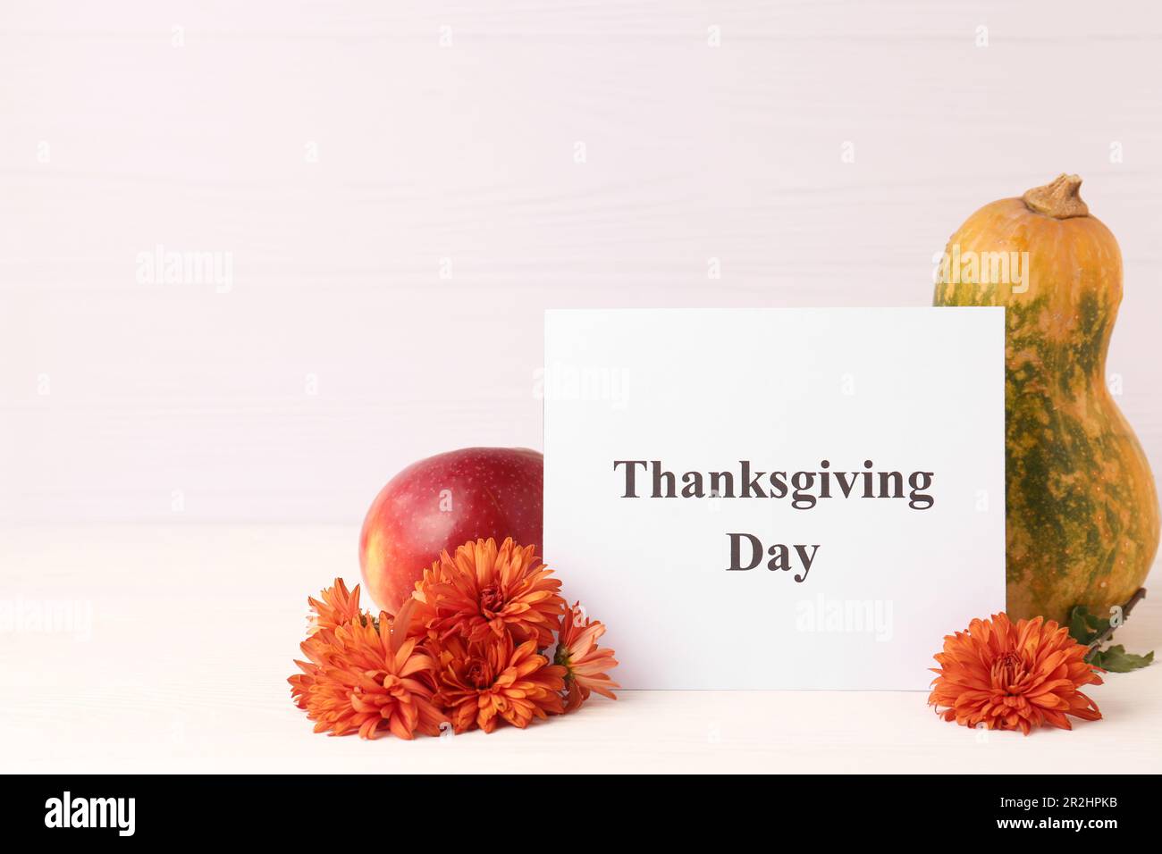 Jour de Thanksgiving, fête célébrée chaque quatrième jeudi de novembre. Carte, pomme, citrouille et fleurs de chrysanthème sur table en bois blanc, espace pour Banque D'Images