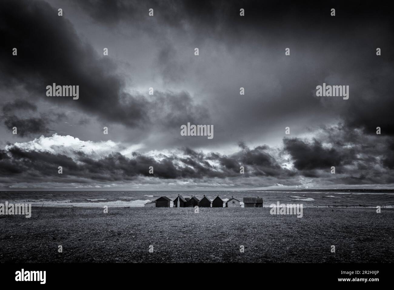 Une rangée de cabanes de pêcheurs seules se trouve sur la plage de pierre. Nuages menaçants dans le ciel. Noir, blanc. Helgumannen fiskelage. Faroe, comté de Gotland, Swe Banque D'Images