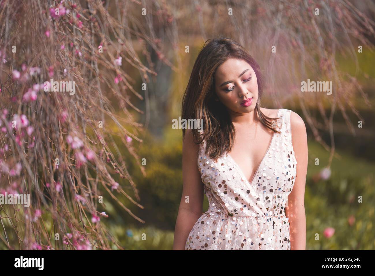 Belle jeune femme en vert rose debout sous le cerisier d'higan pleurant | jardin | fin d'après-midi Banque D'Images