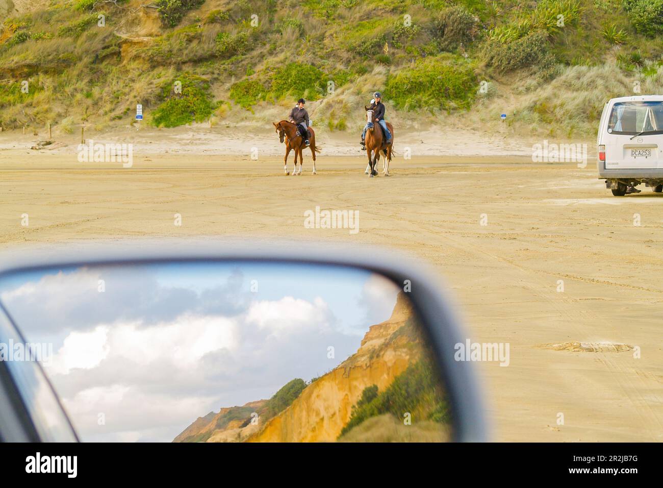 Bayleys Beach New Zealand 6 mars 2011; deux chevaux et des cavaliers sur la plage avec des dunes reflétées dans le rétroviseur de vision arrière de voiture. Banque D'Images