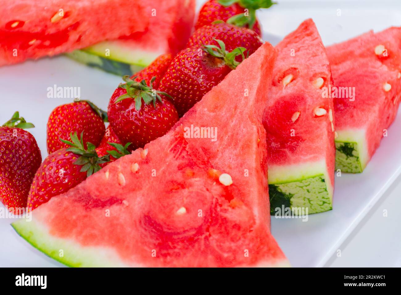 Tranches de pastèque avec plusieurs fraises sur une assiette. Fruits d'été, frais et savoureux Banque D'Images