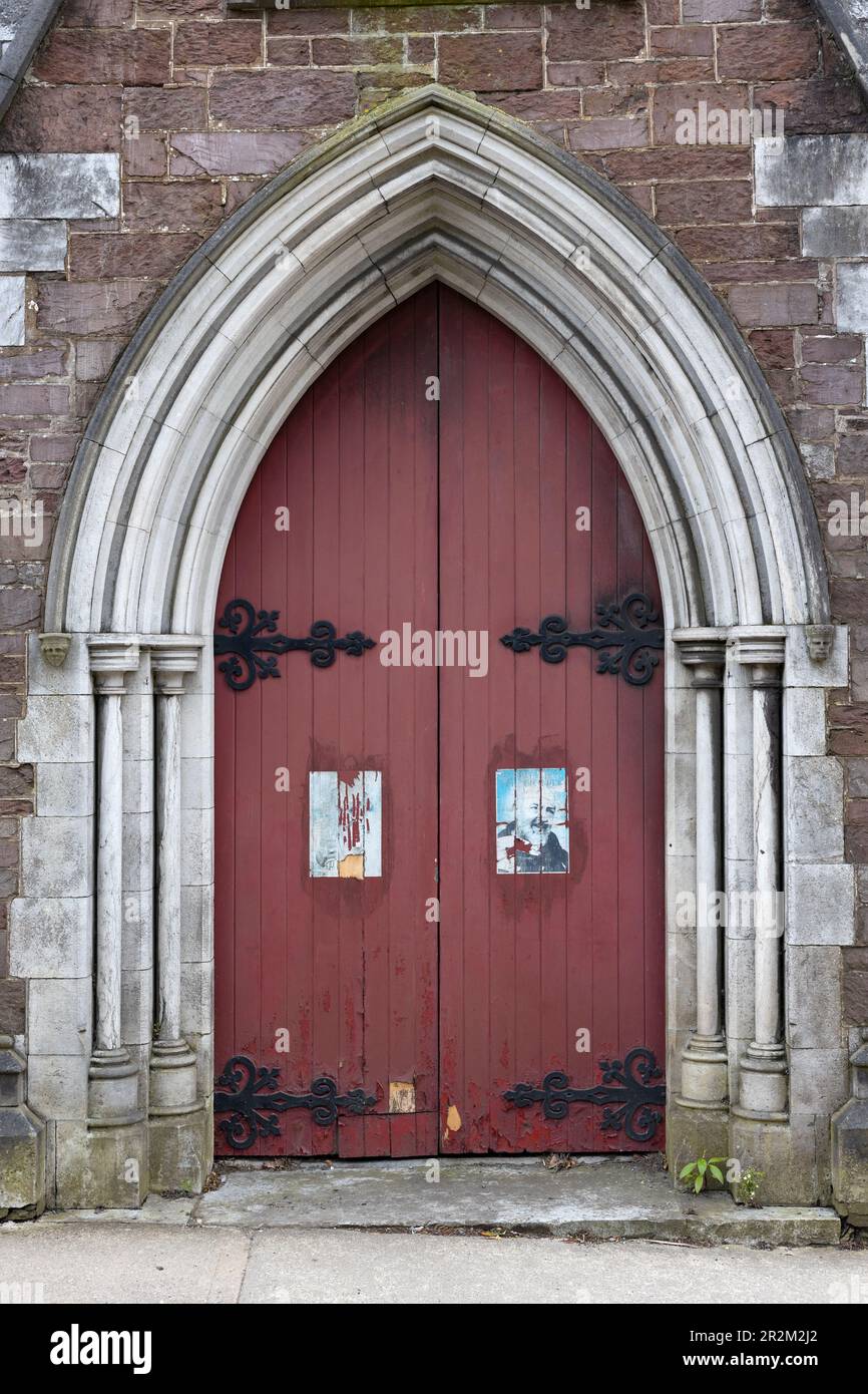 Grandes portes doubles rouges avec affiches usées collées sur elles, à St. Église catholique de Vincent à Cork, en Irlande. Banque D'Images