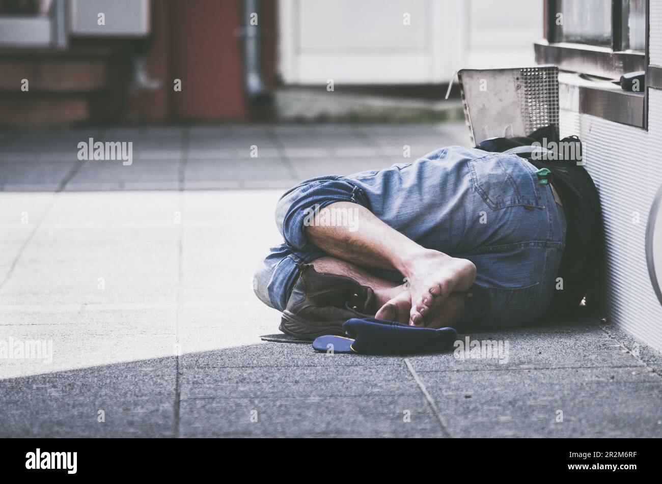 Pauvre fatigué déprimé sans-abri homme ou réfugié dormant sur le banc en bois sur la rue urbaine dans la ville, concept social documentaire Banque D'Images