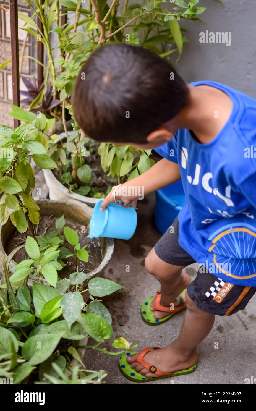 Mignon petit garçon asiatique de 5 ans arrose la plante dans les pots situés sur le balcon de la maison. Amour du petit garçon doux pour la nature de la mère pendant W Banque D'Images