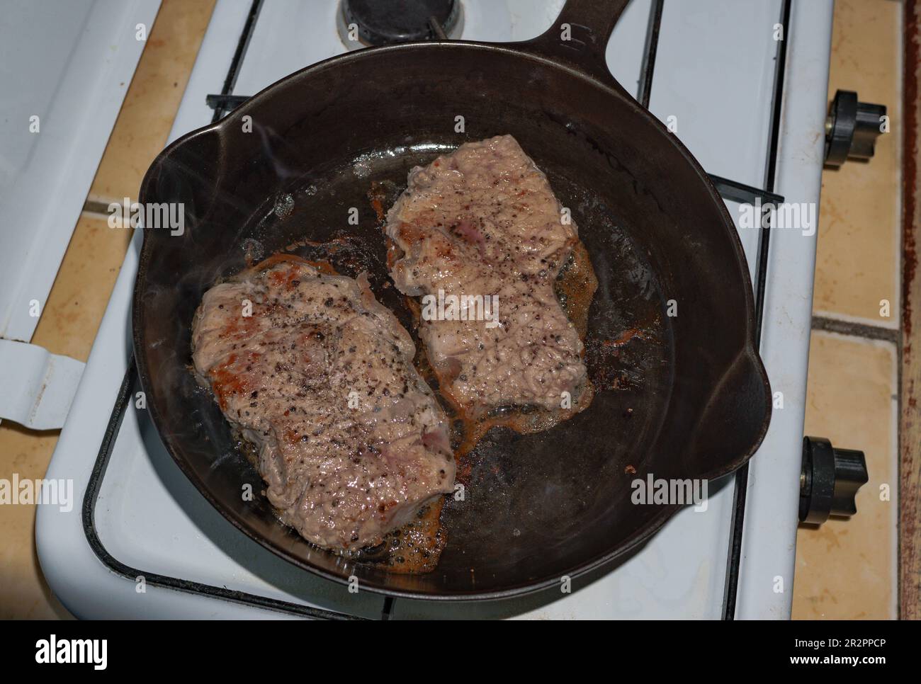 Deux steaks de longe cuisent dans une poêle en fonte sur une table de cuisson au gaz à Jinotega, Nicaragua Banque D'Images