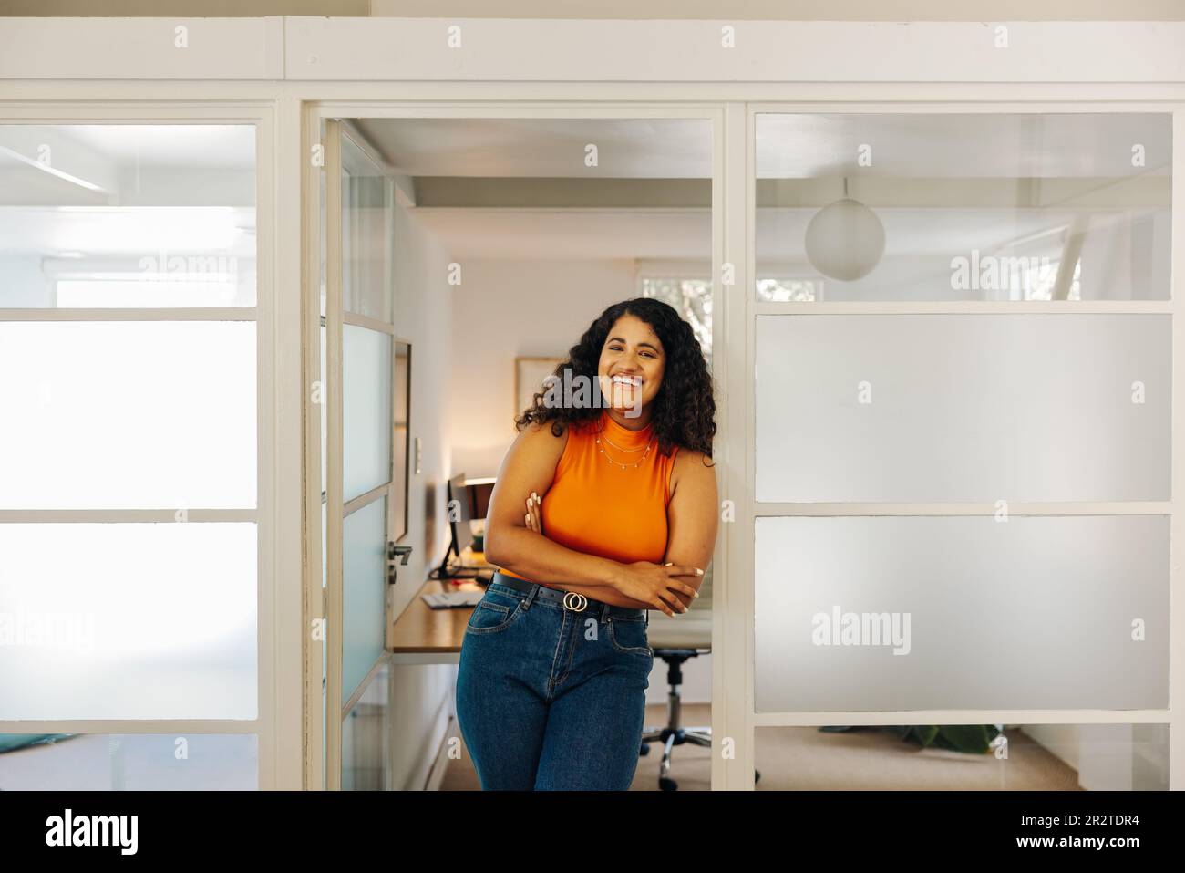 Bonne jeune femme d'affaires souriant à l'appareil photo tout en se tenant devant son bureau. Femme entrepreneure prospère travaillant dans un milieu de travail créatif. Banque D'Images