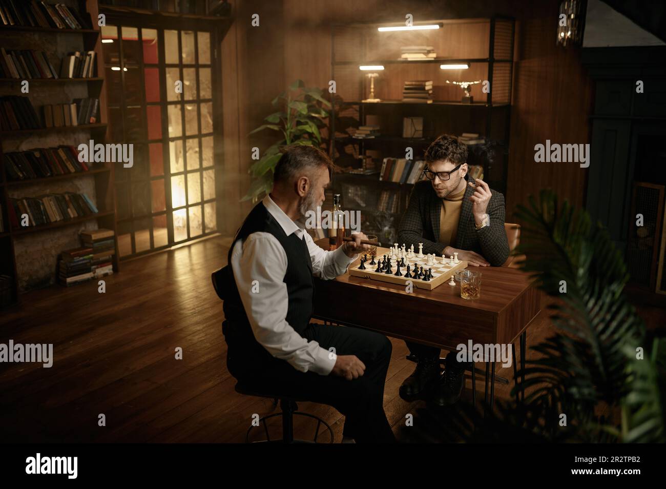 Deux hommes jouant aux échecs assis à table dans le salon de la maison Banque D'Images
