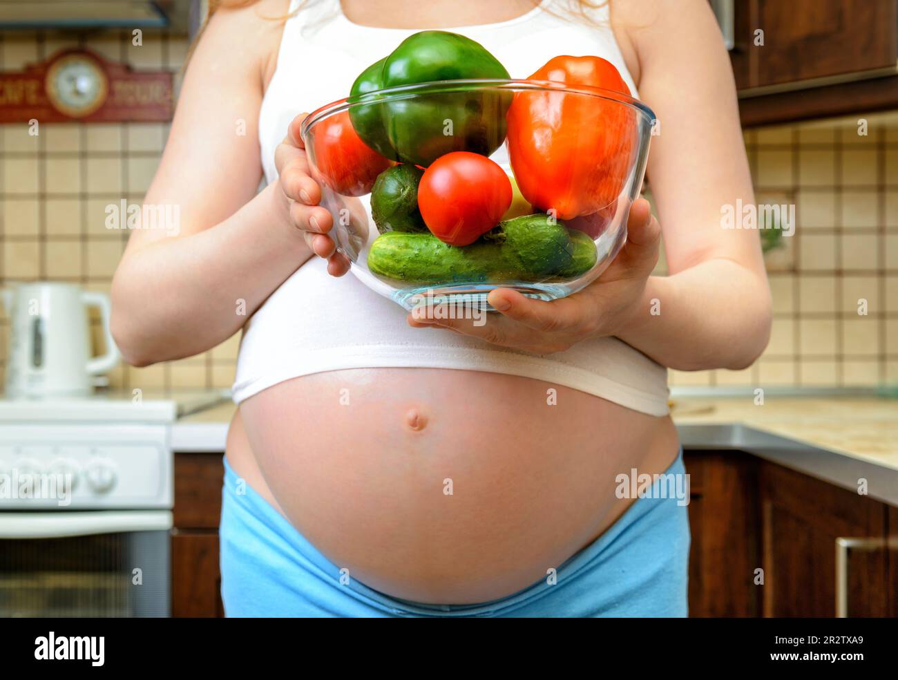 Femme enceinte et alimentation saine dans la cuisine, légumes frais dans les mains. Vue de face d'une femme avec un grand ventre contenant de la nourriture. Concept de grossesse Banque D'Images