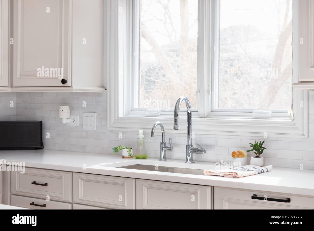 Un détail d'évier de cuisine avec armoires bronzées, comptoir en marbre blanc, dosseret en tuile de métro et robinet chromé. Banque D'Images