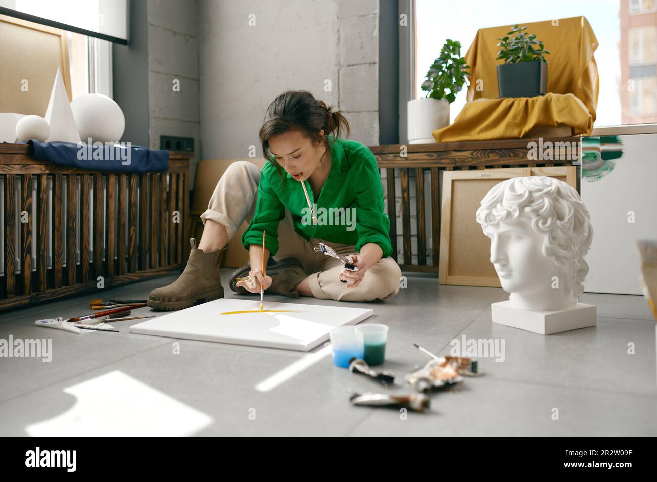 Jeune artiste femme qui dessine une image assise sur le sol dans son propre studio d'art Banque D'Images