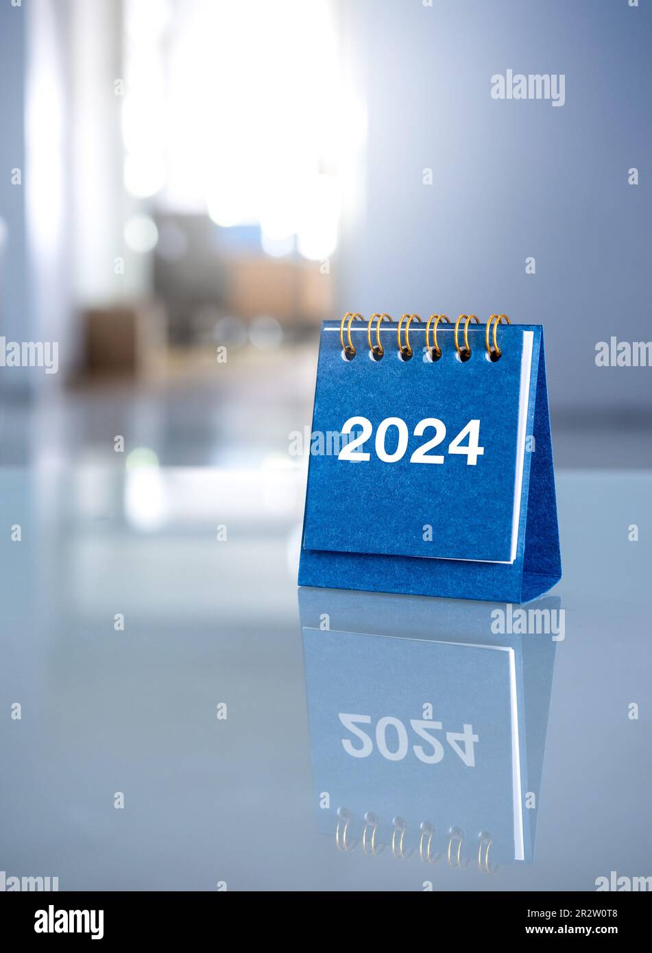 Bonne année 2024. 2024 numéros de l'année sur un petit calendrier bleu sur une table en verre sur un lieu de travail de bureau avec espace de copie, verti Banque D'Images