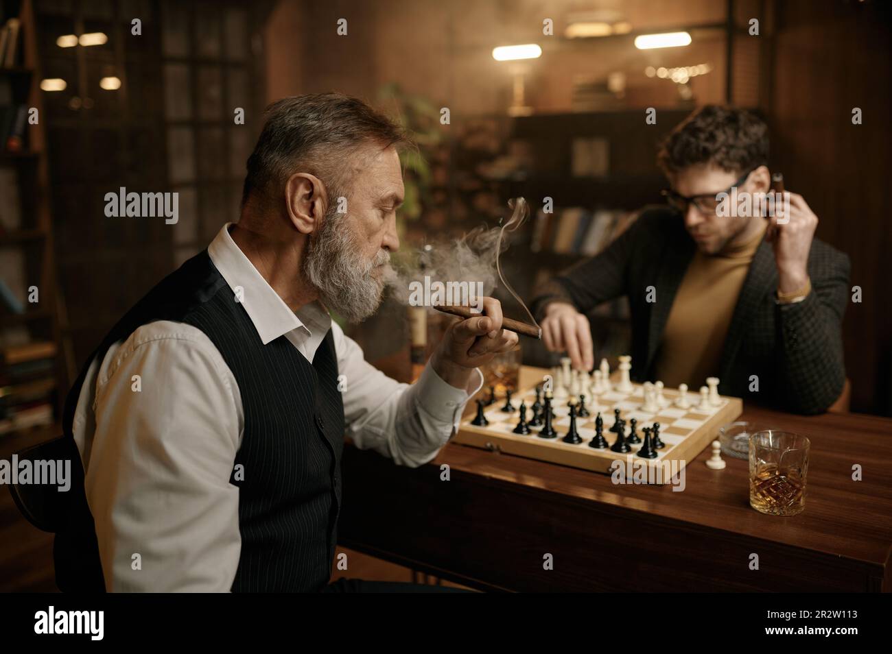 Deux hommes jouant aux échecs assis à table dans le salon de la maison Banque D'Images
