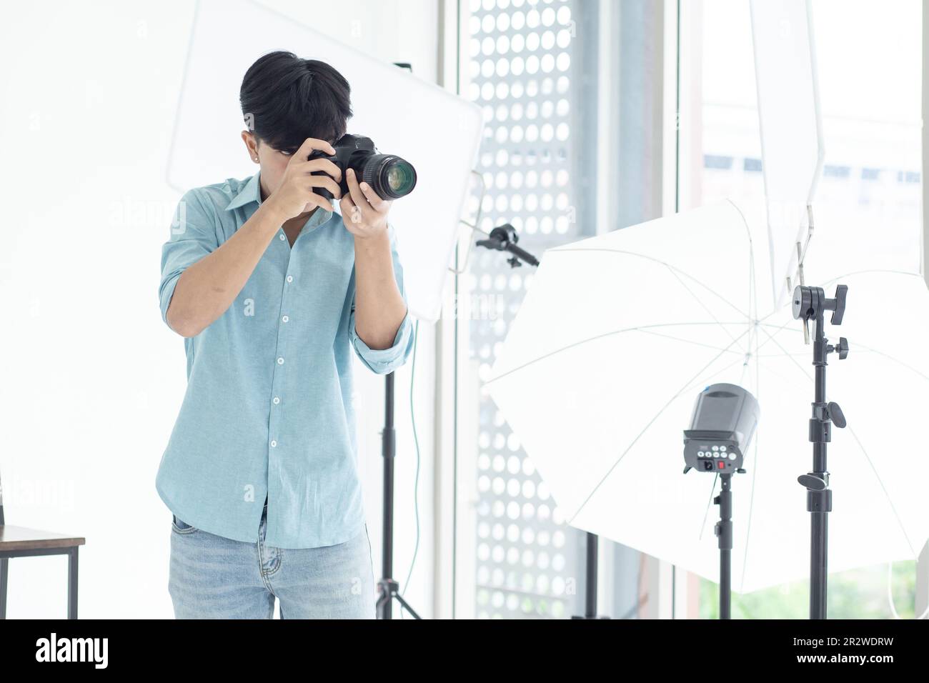 Un photographe asiatique de sexe masculin debout et photographié dans son studio. Avec des lumières studio comme toile de fond et espace de copie. Banque D'Images