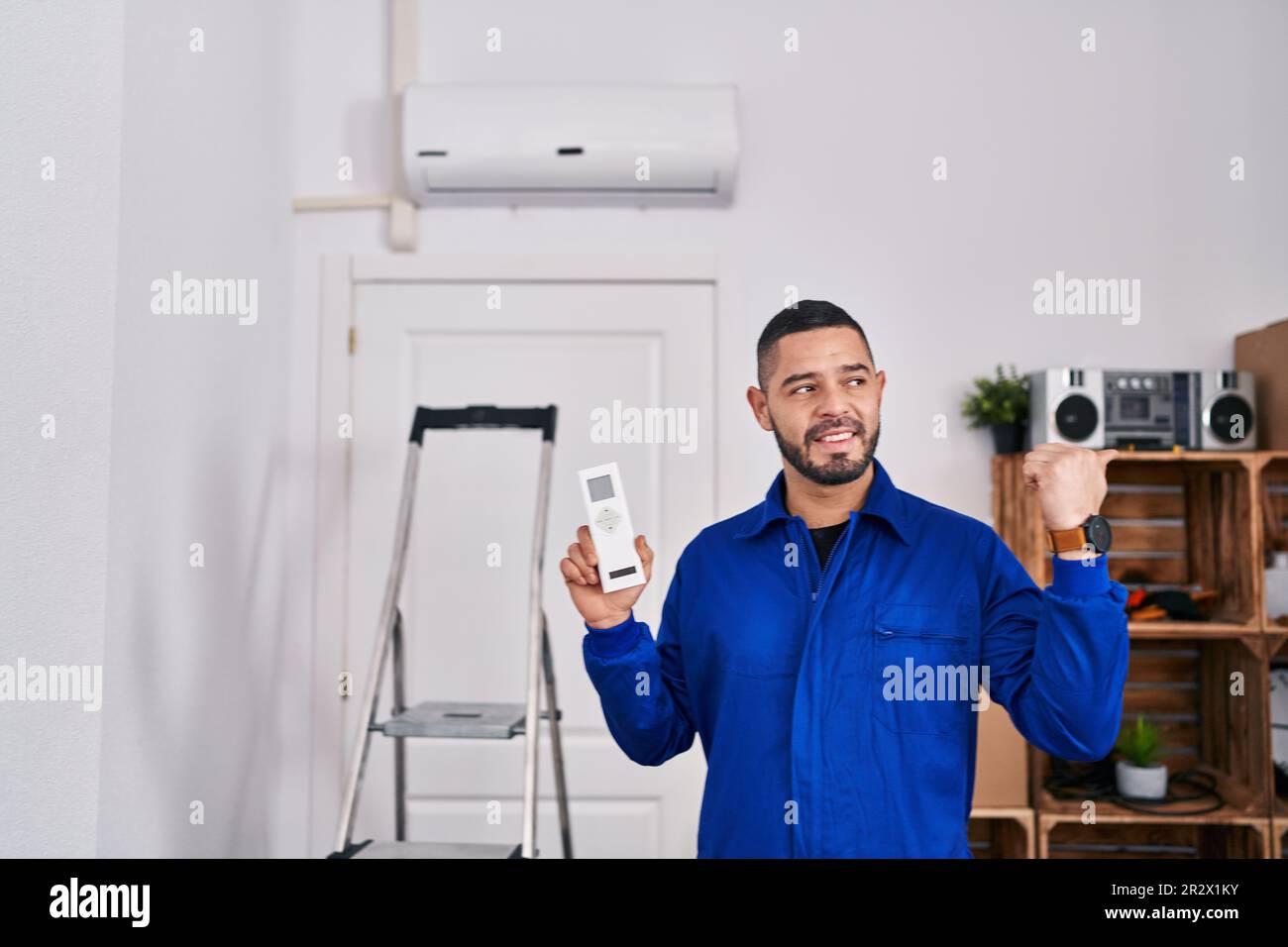 Réparateur hispanique travaillant avec le climatiseur pointant le pouce vers le haut du côté souriant heureux avec la bouche ouverte Banque D'Images