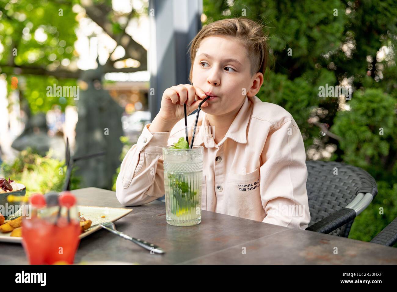 Un adolescent buvant un cocktail dans un café en plein air par temps ensoleillé Banque D'Images
