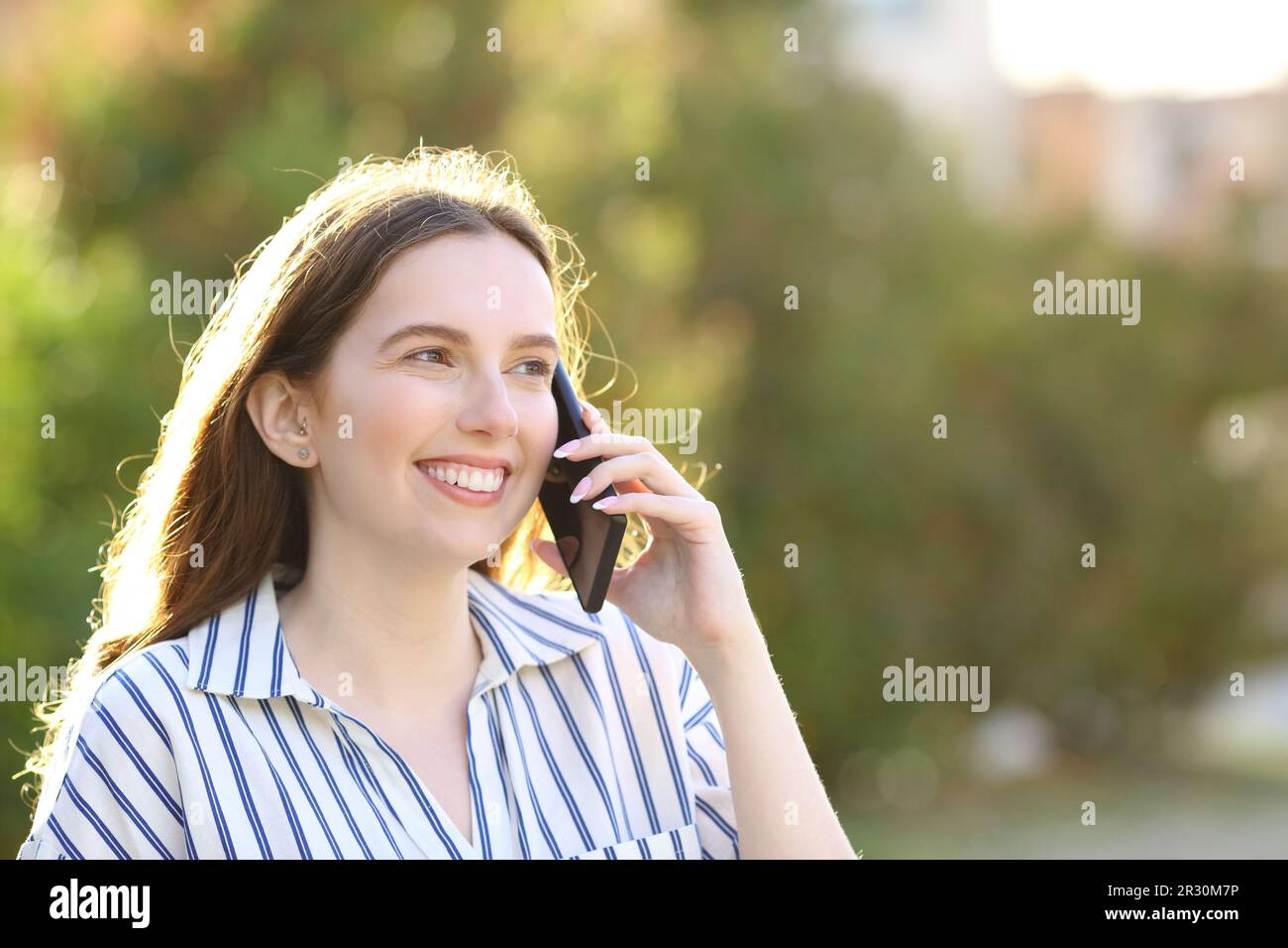 Une femme heureuse parlant sur un téléphone cellulaire marchant dans un parc Banque D'Images