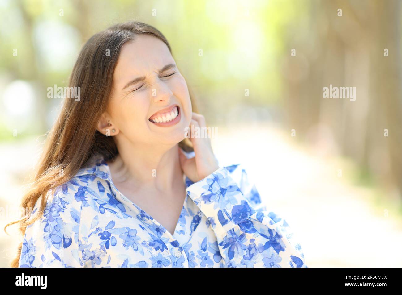 Une femme stressée se grattant le cou dans un parc l'été Banque D'Images