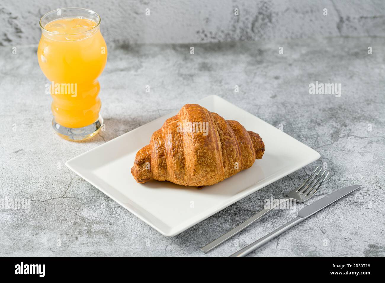 Croissant sur une assiette en porcelaine blanche sur une table en pierre légère Banque D'Images