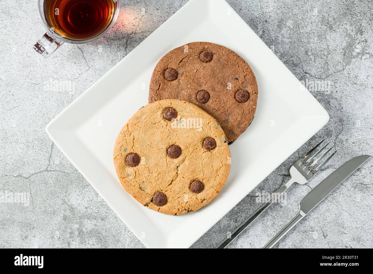 Biscuit aux pépites de chocolat emballé dans un sac en papier avec une boisson à côté sur une table en pierre Banque D'Images