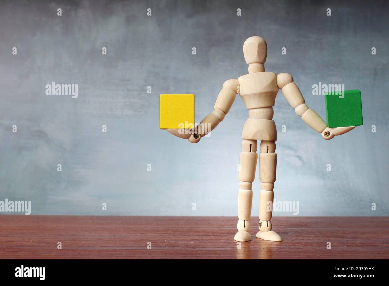 Figure humaine en bois équilibrant cube en bois vert et jaune avec espace de copie pour le texte. Harmonie, stabilité et concept de comparaison Banque D'Images