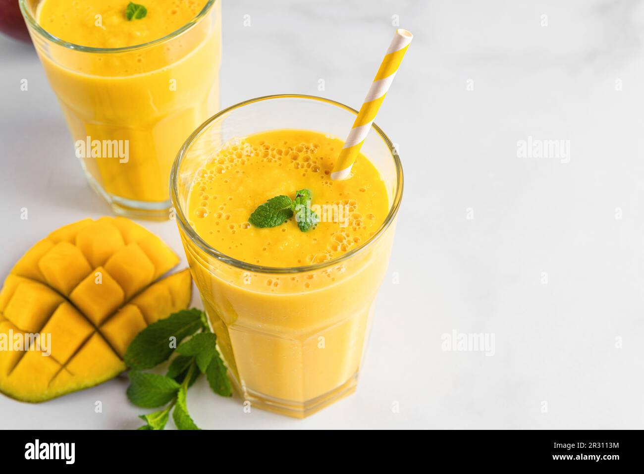 Smoothie à la mangue jaune frais dans des verres avec paille, fruits frais et menthe. Boisson tropicale d'été Banque D'Images
