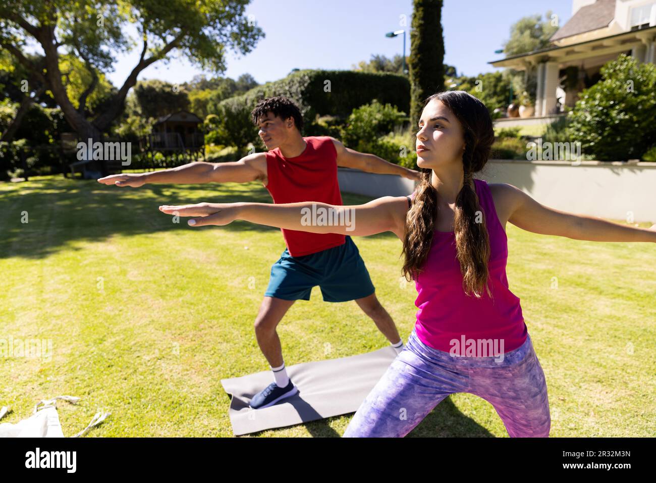 Joyeux couple de forme diverse pratiquant le yoga debout et s'étirant dans le jardin ensoleillé Banque D'Images