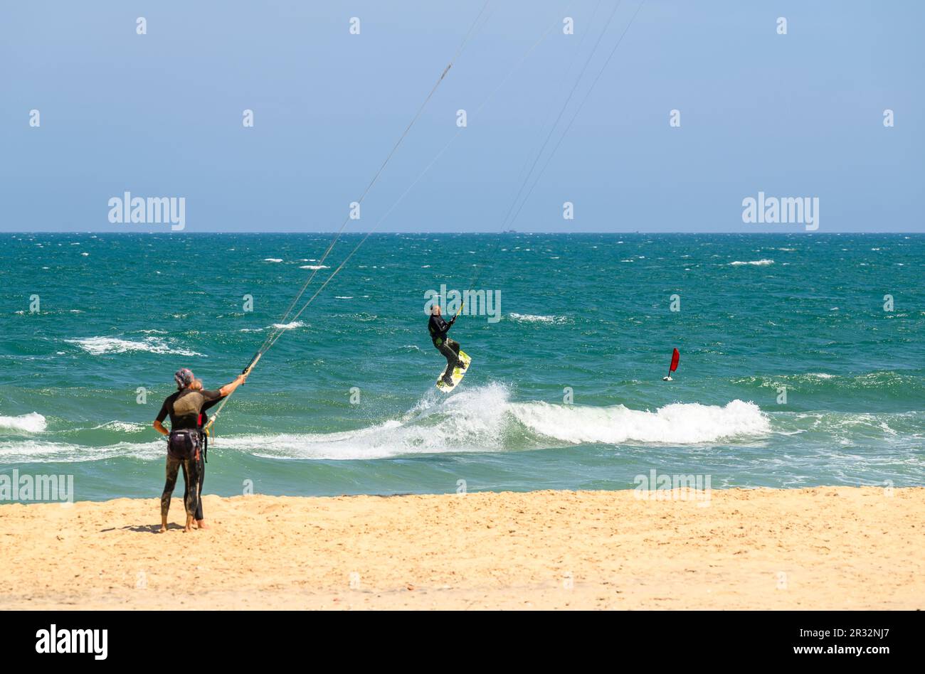Instructeur et apprenant tenant des lignes de cerf-volant tandis qu'un kitesurfer saute dans les airs avec un double conseil de la plage à Mui ne, Vietnam. Banque D'Images