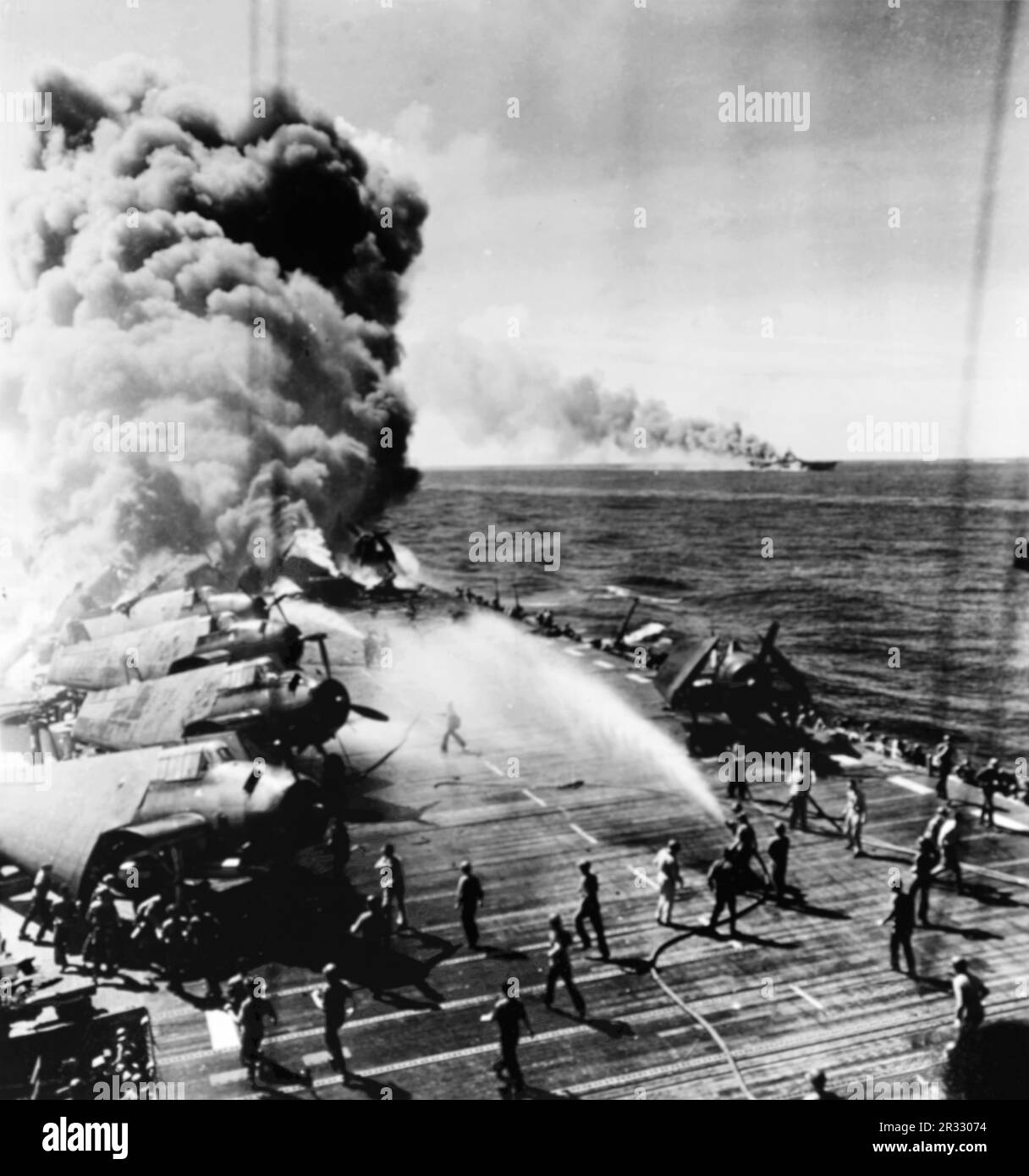 États-Unis Le porte-avions léger USS Belleau Wood (CVL-24) de la Marine a brûlé en arrière après avoir été frappé par un kamikaze, alors qu'elle a été en opération au large de Luzon, aux Philippines, le 30 octobre 1944. Les membres de équipage du pont de vol déplacent les avions Grumman TBM Avenger intacts du Torpedo Squadron 21 (VT-21) loin des flammes tandis que d'autres combattent les incendies. L'USS Franklin (CV-13), également touché lors de cette attaque de Kamikaze, est à l'écart. Banque D'Images