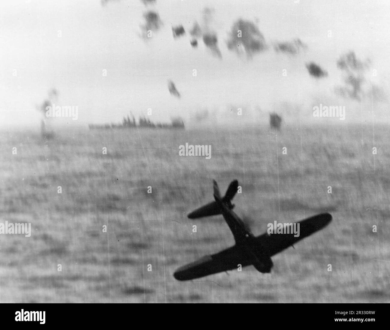 Japonais Mitsubishi A6M5 Zero Kamikaze combattant avant de s'écraser dans la mer après avoir essayé de frapper les États-Unis Le porte-avions de la Marine USS Essex (CV-9) au large d'Okinawa, en 1945. Notez le croiseur léger de classe Cleveland en arrière-plan. Banque D'Images