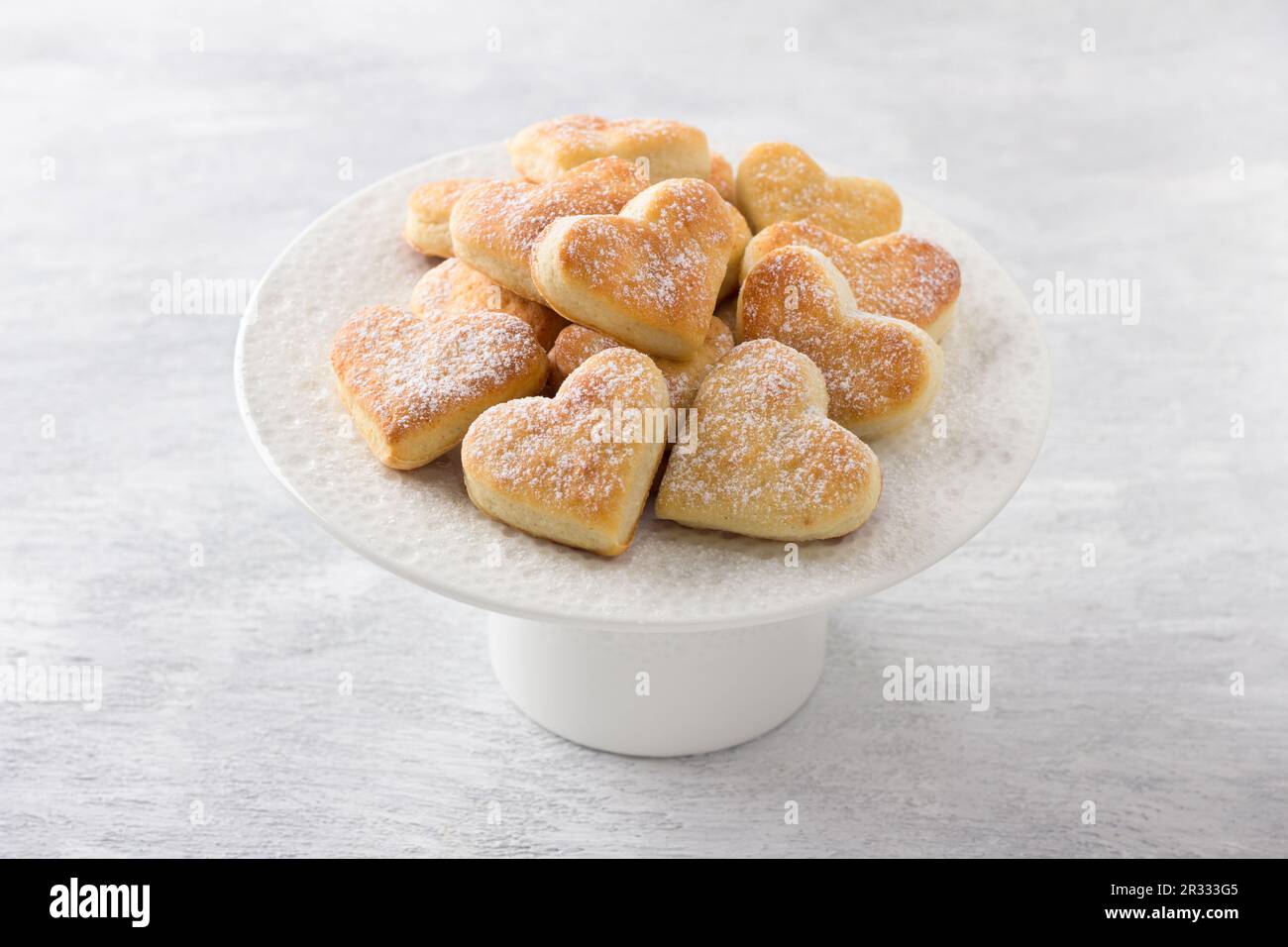 Biscuits au lait caillé doux arrosé de sucre en poudre sur une plaque blanche sur fond gris clair. Délicieux petits gâteaux faits maison Banque D'Images