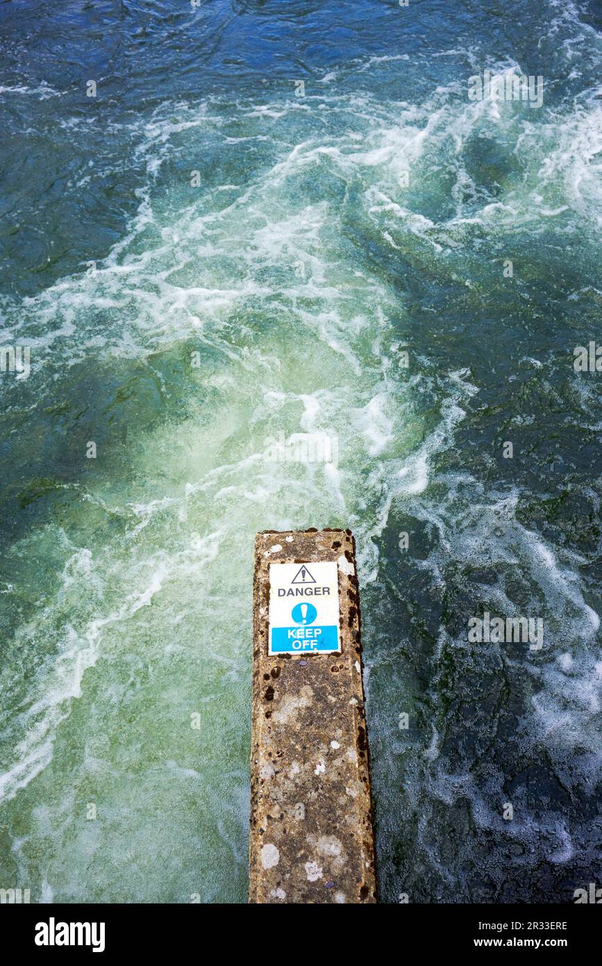 L'eau se précipitant au-delà d'une jetée en béton avec un panneau danger Banque D'Images