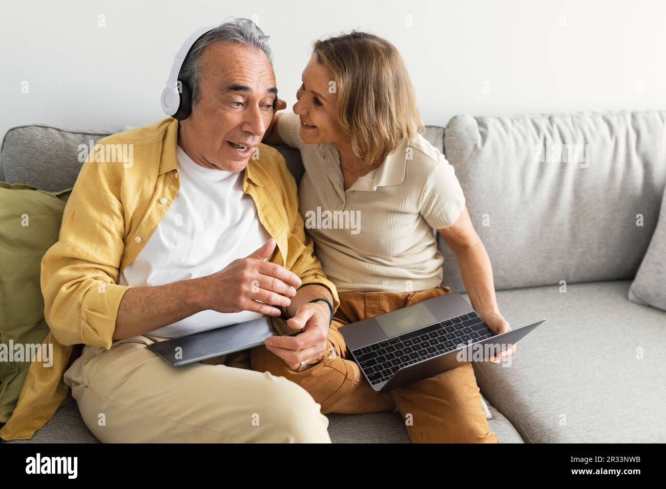 Un homme âgé qui écoute de la musique dans un casque sans fil, une femme qui lève l'écouteur et parle dans l'oreille de son mari Banque D'Images