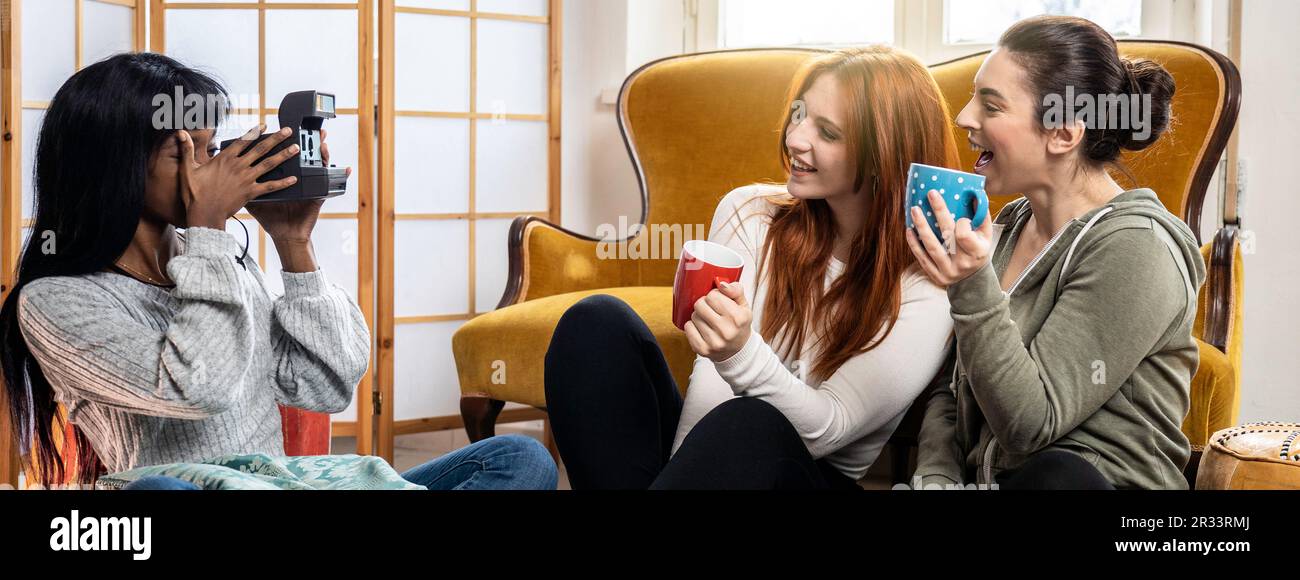 Bannière horizontale ou en-tête avec des amies multiculturelles heureuses appréciant du temps libre ensemble à la maison - jeunes femmes tout en buvant du café ou du thé et Banque D'Images