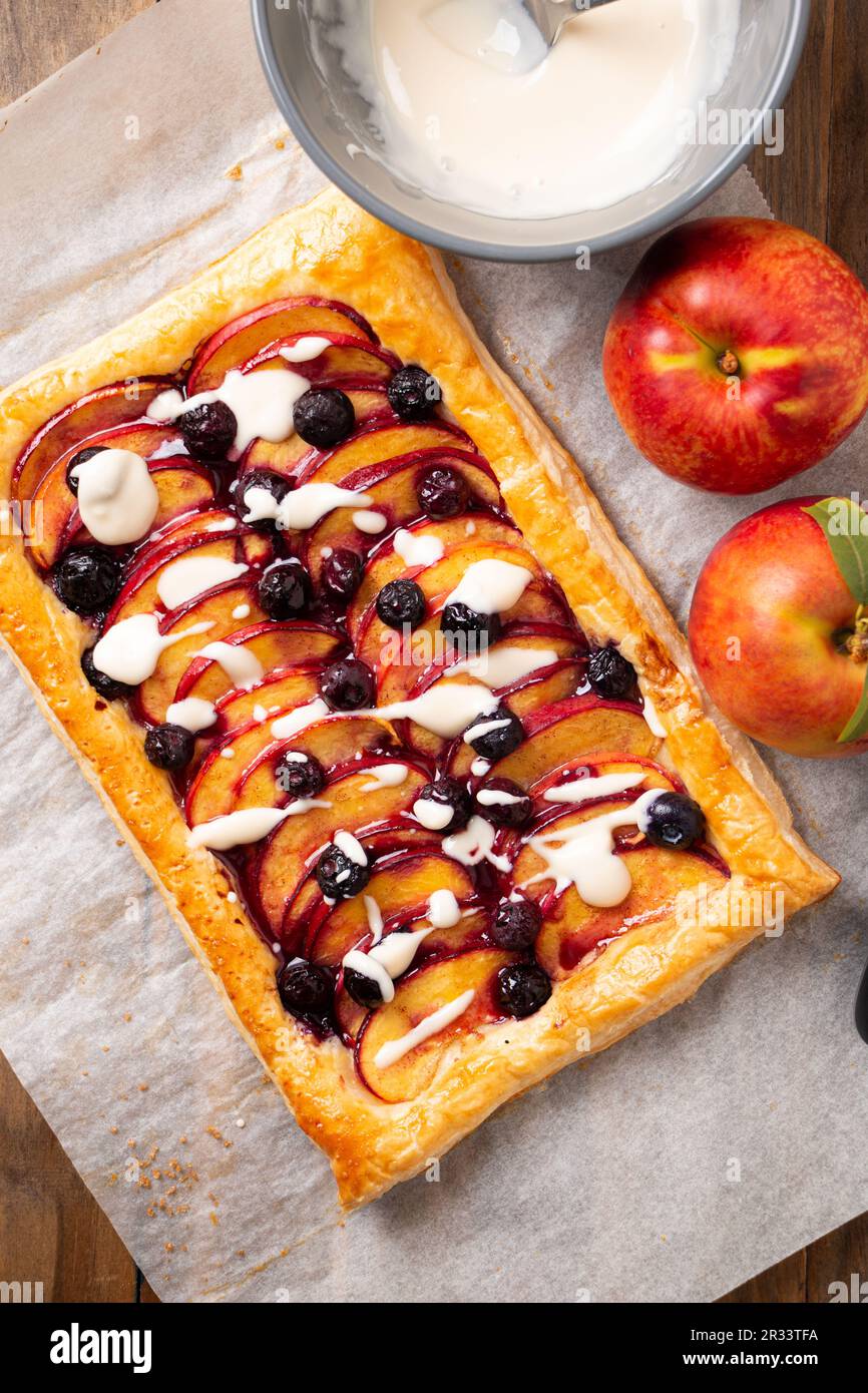 Tarte feuilletée à la nectarine et aux myrtilles avec glaçage à la vanille sur un papier à pâtisserie Banque D'Images