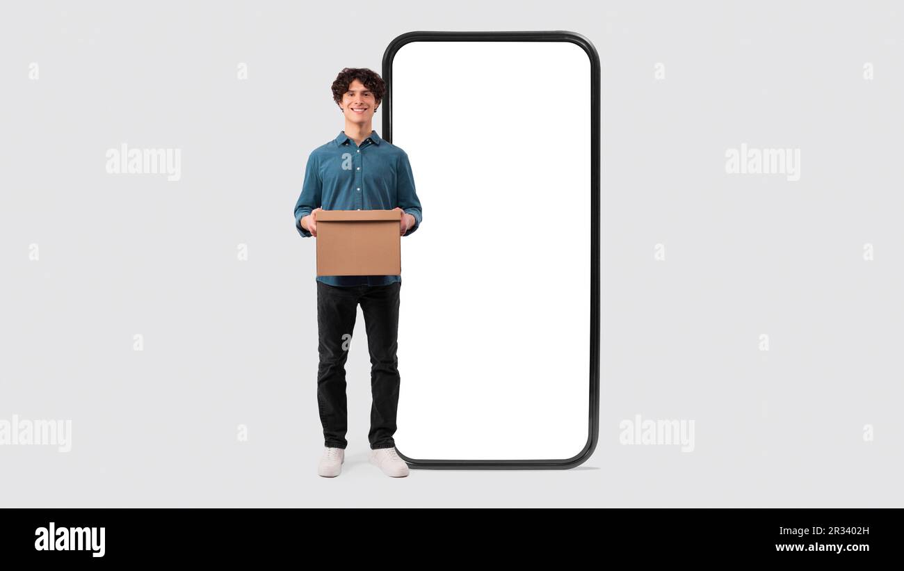 Homme tenant une boîte en carton près d'un immense téléphone sur fond blanc Banque D'Images