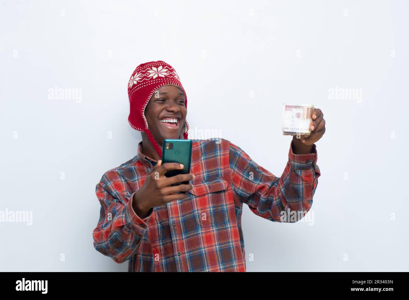 un jeune africain enthousiaste tenant de l'argent et utilisant son téléphone se réjouit Banque D'Images