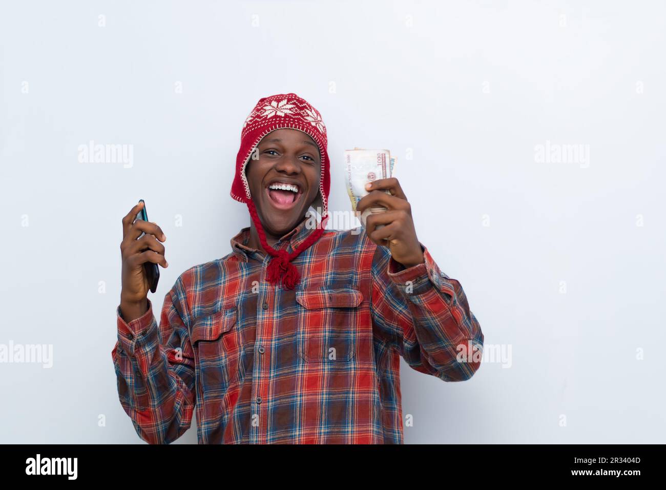 un jeune africain enthousiaste tenant de l'argent et utilisant son téléphone se réjouit Banque D'Images