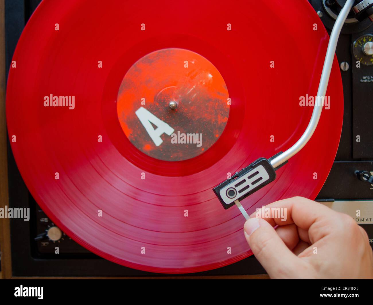 Détail d'une main masculine plaçant l'aiguille sur la piste d'un disque en vinyle rouge. Plateau tournant vintage Banque D'Images